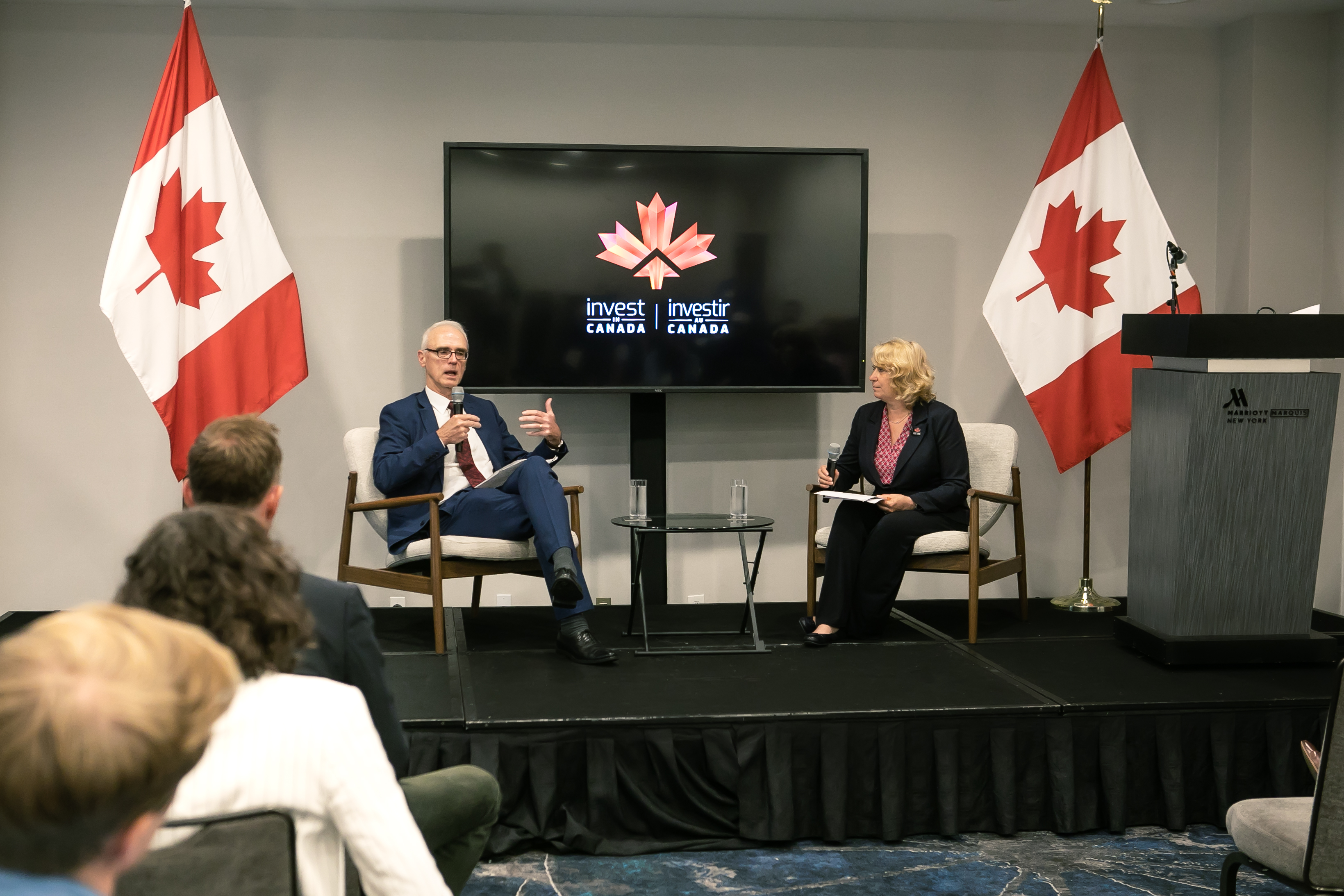 Two people on stage having a discussion with Canada flags in the background