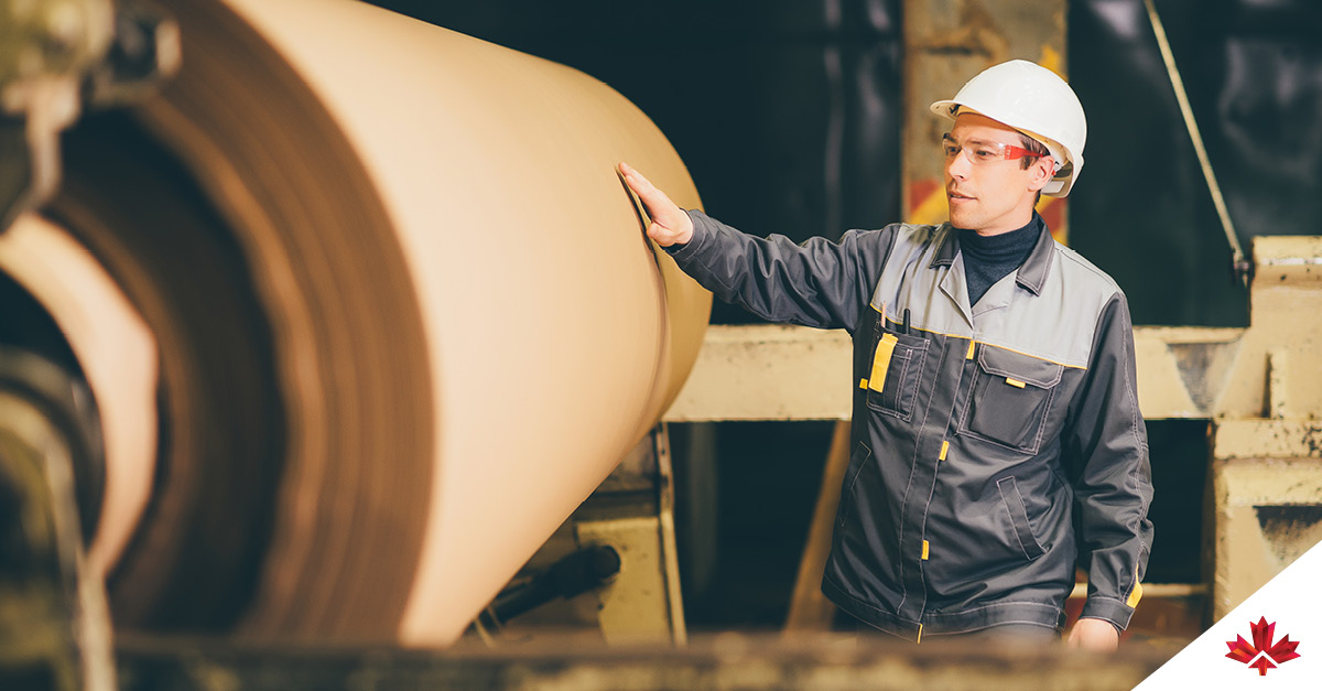 A paper mill employee is stationed at a kraft paper machine, wearing protective equipment. 