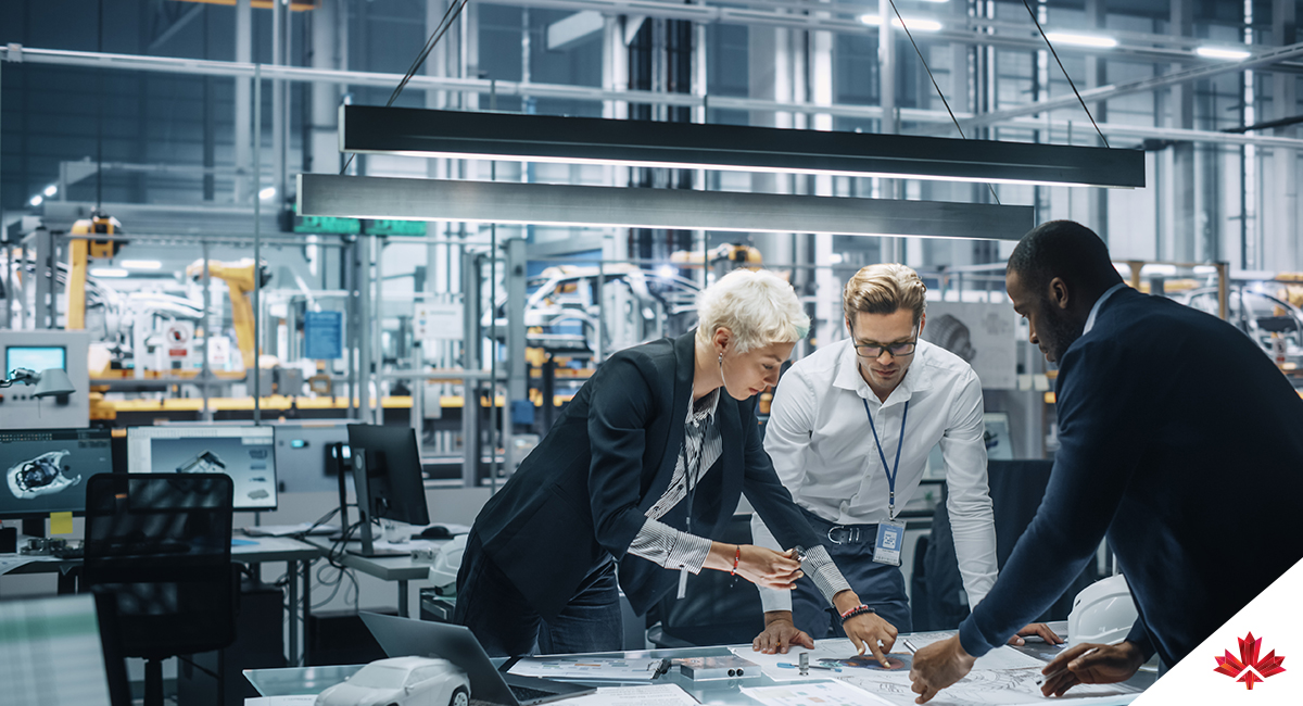 A group of workers look over a table at a chart in a factory setting.