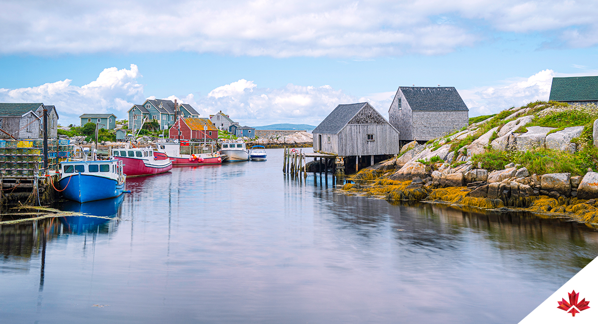 Peggy’s Cove’s seascape with blue and red boats and weathered seaside shacks on each side of the shore.