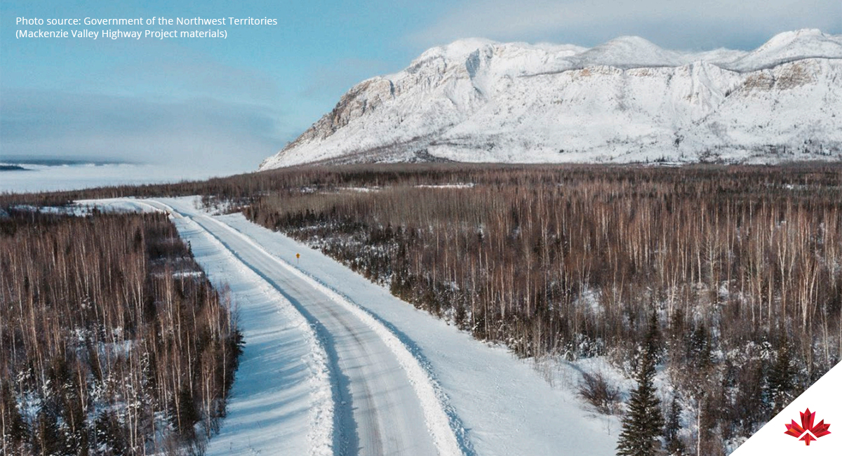 Snow-covered seasonal road through northern forest landscape in the Northwest Territories with mountains in the distance.