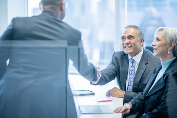Hands of Asian African-American mature businessmen shaking hands in bright business office during meeting wearing suits
