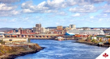 Landscape of Saint John, New Brunswick, including office and commercial buildings, transportation infrastructure, and a body of water and both large and small boats. 