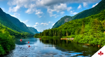 Lush greenery, waterway and sky above the Jacques-Cartier river in Québec, Canada with kayakers on the water.