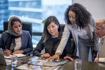 Professional reviewing business documents at a desk, holding a pen and analyzing paperwork.