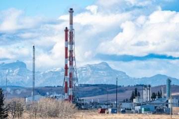 Oil and gas plant with tall flare stacks overlooking distant Canadian Rockies near Cochrane, Alberta, Canada.