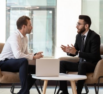 Middle eastern and caucasian ethnicity businessmen seated on armchair in modern office talking
