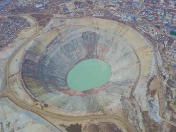 A large circular open‑pit diamond mine viewed from above, with terraced layers of earth surrounding a greenish‑blue pool at the center.