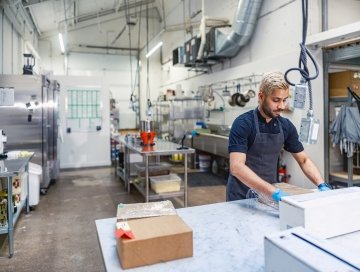 Indian male chocolatier working at the chocolate factory. He is dressed in work uniform. Interior of large kitchen at the chocolate factory during the day in Toronto, Canada.