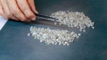 Assortment of diamonds on a dark background with a hand sorting them.