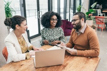 Group of multiracial business people sitting at a table discussing and looking at plans with a laptop. 