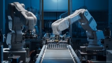 Robotic arms assembling components on a black circuit board along an automated PCB production line.