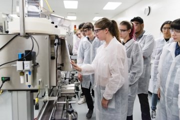 Multi-ethnic group of new College students being introduced to pharmaceutical laboratory equipment. Large groupe of people. They all are wearing protective work gear, glasses and lab coats. 