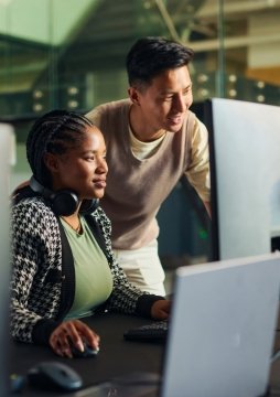 Software engineers working together and analyzing code on multiple computer monitors in an office setting.