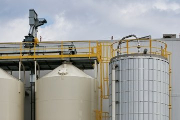 Close-up street level view of industrial storage silos with yellow metal ladders and pipes, photographed in Saskatoon, Canada.