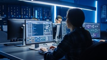 IT professional working at a computer workstation inside a data center control room.