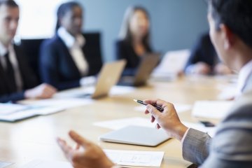 Hands of businessman gesturing ideas decisions with pen pointing leadership to work colleagues in business meeting at board room conference table.