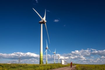 Giant wind generators showing size comparison with technician on ground.