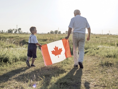 child and elderly man walking in field holding a Canada flag